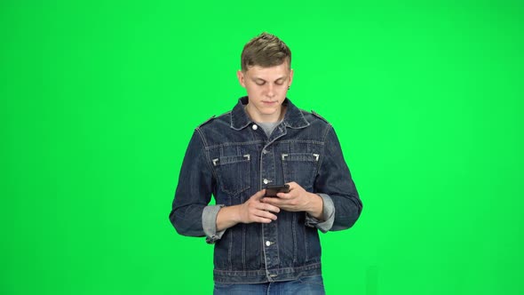 Smiling Man Goes and Texting with Smartphone on Green Screen at Studio