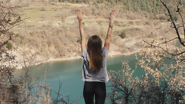 Young Woman Stands with Raised Arms Up on the Nature Lake Sunset Background