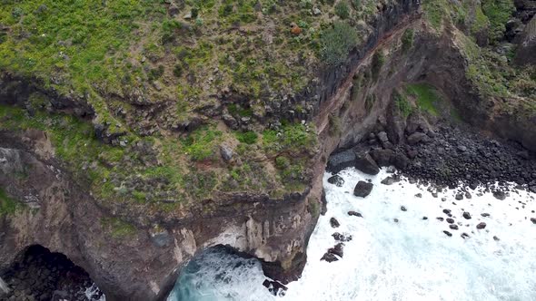 Top-down birdseye aerial drone view of dramatic cliffs dropping into the stormy ocean. Clip recorded