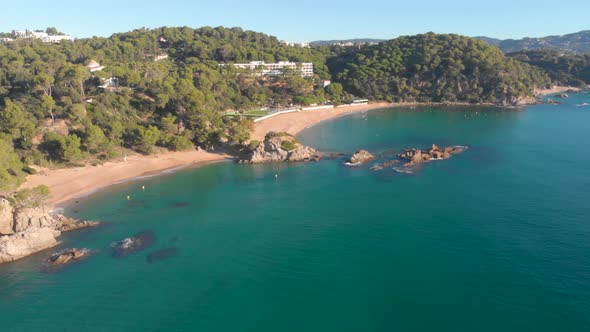 Aerial, drone shot, over rocky coast and turquoise sea, towards Lloret de Mar beach, Santa Cristina,