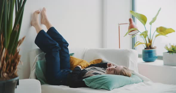 Young woman laying on couch looking bored with her legs up against the wall