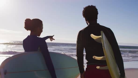 African american couple talking and carrying surfboards on the beach