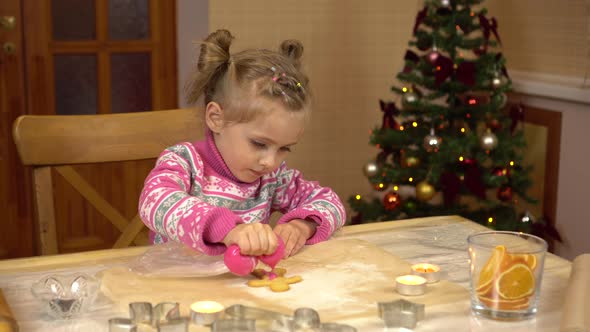 A Girl Decorates a Gingerbread Human Shaped Cookie with Pink Icing. The Child Is Preparing for