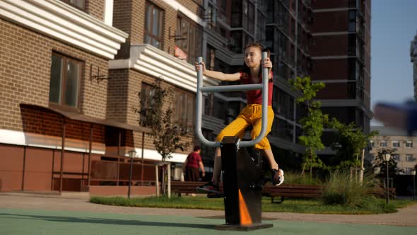 A 10Yearold Girl is Doing Sports in the Courtyard of the House on a Street Exercise Bike