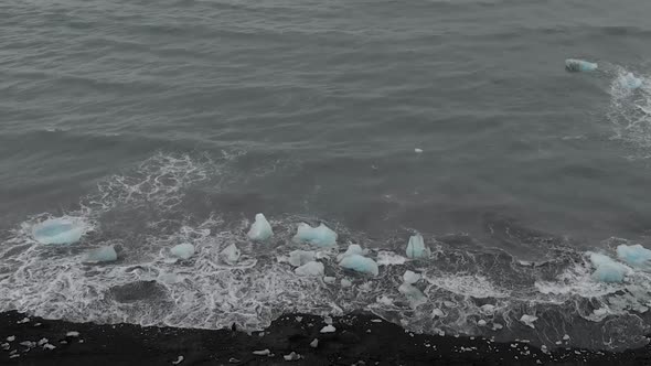 Slow motion panning shot of waves crashing into icebergs.