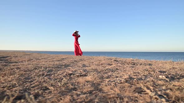 A Romantic Woman in a Red Dress Stands on the High Seashore