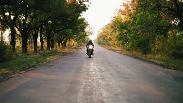 Front View of Stylish Man in Black Helmet and Leather Jacket Riding Motorcycle on an Asphalt Road on