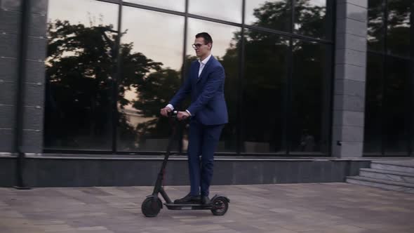 Young Businessman in Elegant Blue Suit and Glasses Riding an Electric Scooter for a Business Meeting