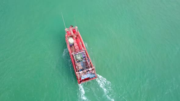 Red Fishing Boat Sails Along the Coast in Turquoise Sea, Aerial View.