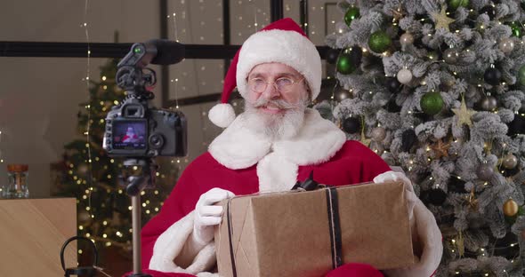 Santa Claus Recording Video Appeal to Children Holding Christmas Gift Box Sitting in Front of