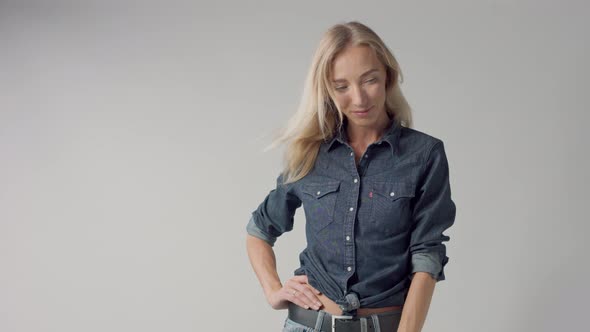 Young Beauty Blonde Woman in Studio Wears Classic Denim with Blowing Hair