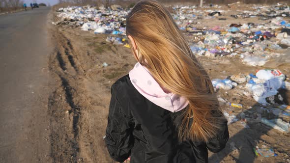 Little Girl Goes on the Road Against the Background of Garbage Dump. Small Female Child with Blonde