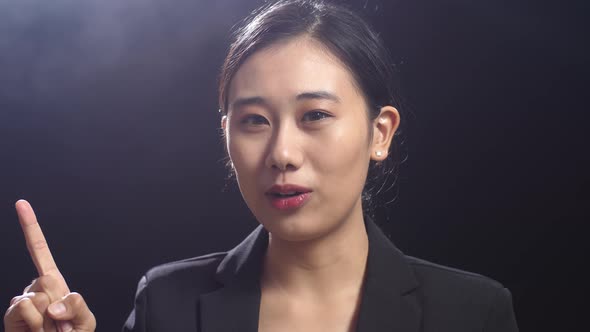 Close Up Of Asian Speaker Woman Showing Index Fingers Up While Speaking In The Black Studio