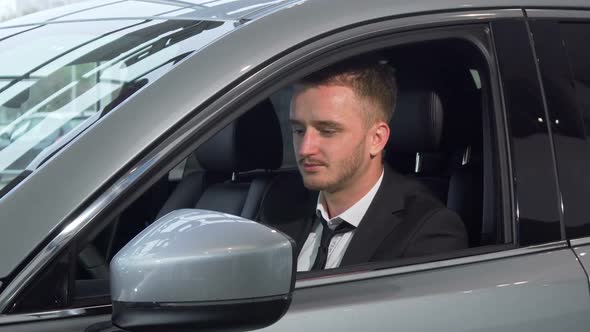 Cheerful Businessman Holding Car Keys Sitting in a New Auto at the Dealership