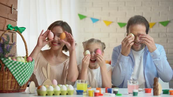 Cheerful Family Having Fun Preparing for Easter and Putting Colored Eggs to Eyes