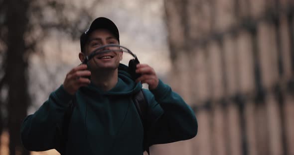 Smiling Man Puts on Headphones Walking in the City