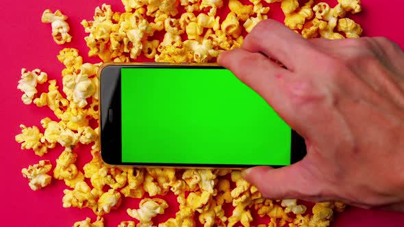 Smart phone with green touch screen and popcorn on red background.