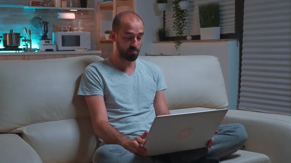 Focused Man Sitting on Sofa in Pajamas While Talking with Collegue During Videocall Conference