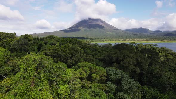 Aerial footage of ascending backwards flight revealing the thick rainforest that surrounds Arenal Vo
