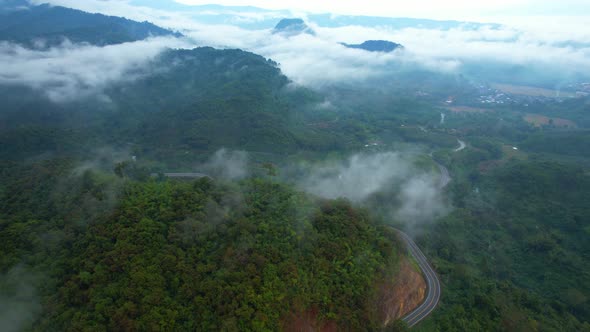 4K Aerial view from a drone flying above rural clouds, road in a tropical forest in Thailand