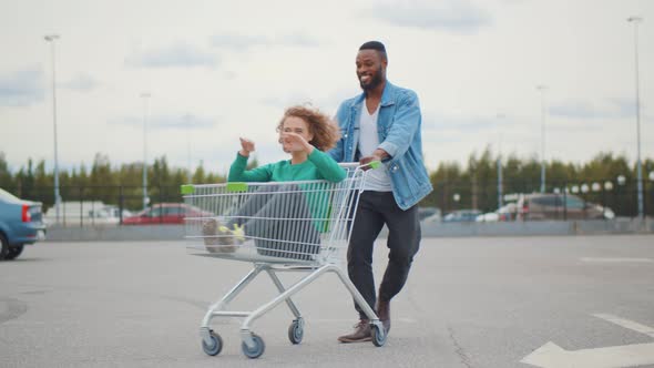Happy African American Man Spinning Girl Sitting in Shopping Cart