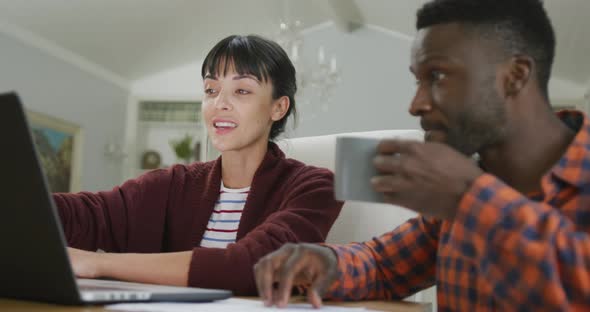 Happy diverse couple sitting at table and working with laptop