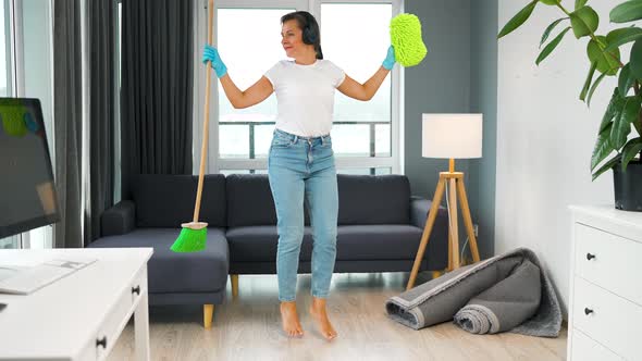 Woman in Headphones Cleaning the House and Having Fun Dancing with a Broom and Washcloth