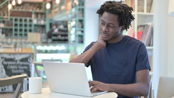 African Man with Neck Pain Working on Laptop in Cafe