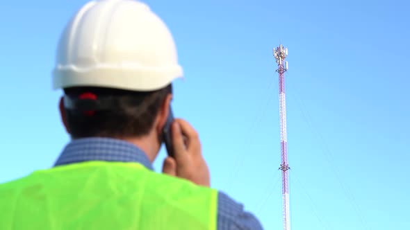 An Engineer Speaks on the Phone Against the Backdrop of a Telecom Tower