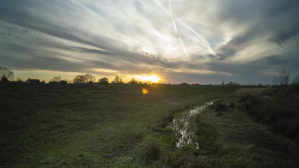 Small dyke near river with vibrant orange sunset sky, time lapse view