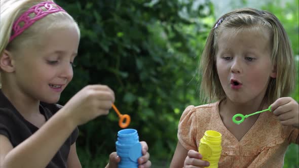 Slow handheld shot of two little girls blowing bubbles