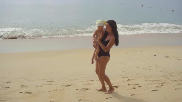 Mom with a Two-year-old Daughter Walking Along the Sandy Beach