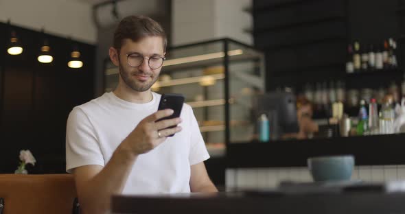 Attractive Serious Man in Eyeglasses Wearing in White Shirt Sitting at Table at Coffee Shop and