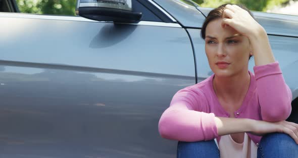 Depressed woman sitting near car
