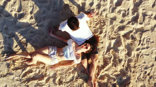 Girl lying on white sand, rested her head on the boy's lap, relaxing on quiet exotic beach at sunris