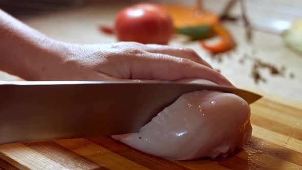 Closeup of Cook Chef Hands Woman Cuts Raw Meat Chicken Breast on a Wooden Board