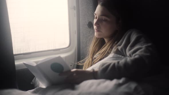 Young female reading book in van