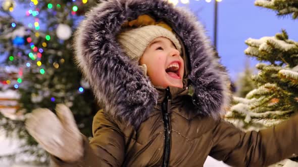 Portrait of happy girl in winter in fur hood against background of fairy lights, Christmas trees