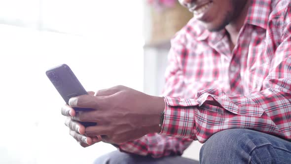 Close up hands African man sitting on sofa, holding smartphone