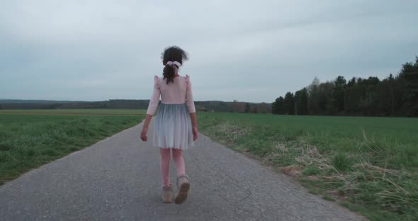 Pan from right to left of little girl walking down empty field road