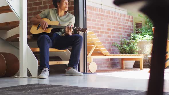 Happy african american man plays guitar and singing at home