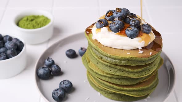 Matcha pancakes with coconut cream, blueberries and pouring maple syrup.