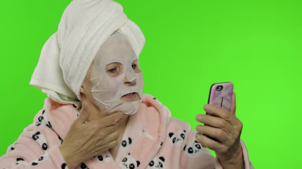 Grandmother in Bathrobe, Face Mask. Old Woman Using Mobile Phone for Video Call
