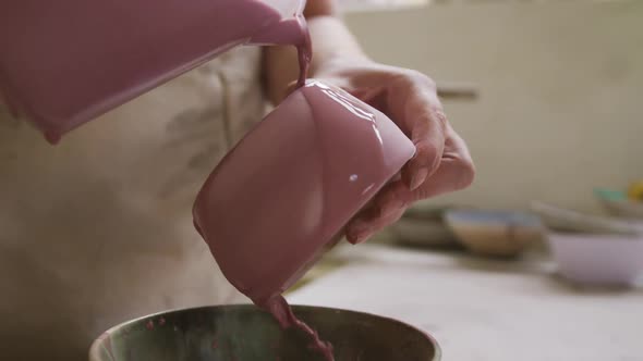 Close up view of female potter pouring paint from a jug on pot at pottery studio