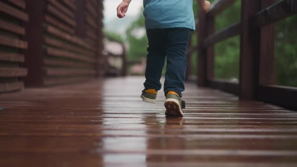 Toddler Boy Runs Along Wet Veranda Deck at Cottage House