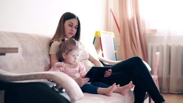 Side View, : Young Attractive Mother and Sweet Daughter Are Sitting on the Couch and Training