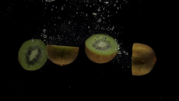 Slow Motion Kiwi Halves Falling Into Transparent Water on Black Background