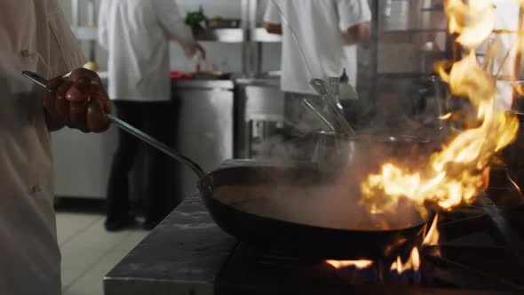 Midsection of african american male chef frying vegetables in pan