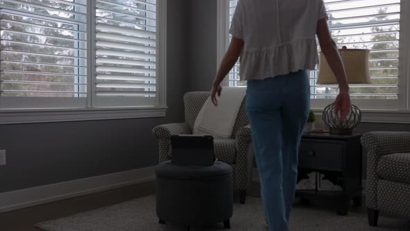 Woman walking to a chair in a corner nook to scroll through her tablet and drink coffee in nice clot