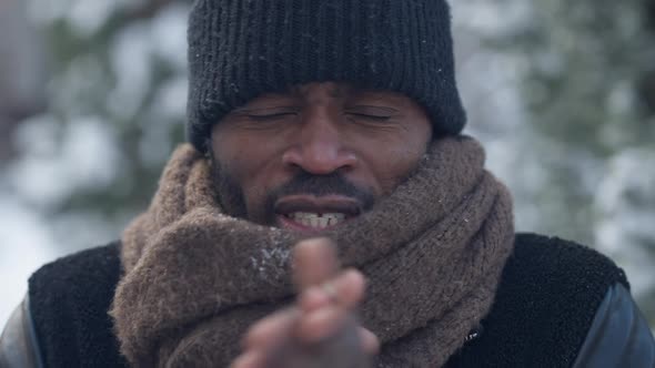 Closeup of Freezed African American Man Blowing on Palms and Rubbing Hands Looking at Camera